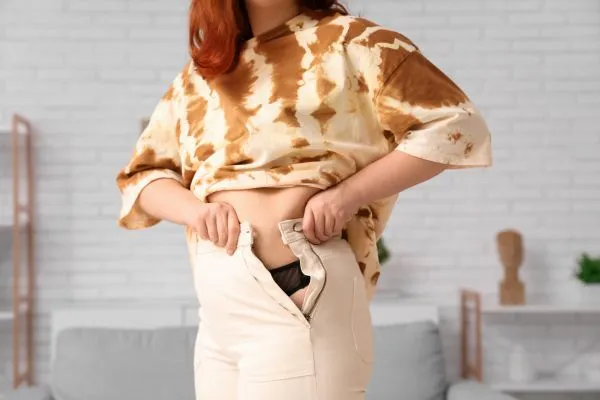 Image of woman trying to do her trousers up after pregnancy weight gain Stansted